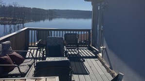 A wooden deck with outdoor furniture, overlooking a calm lake and a distant shoreline.