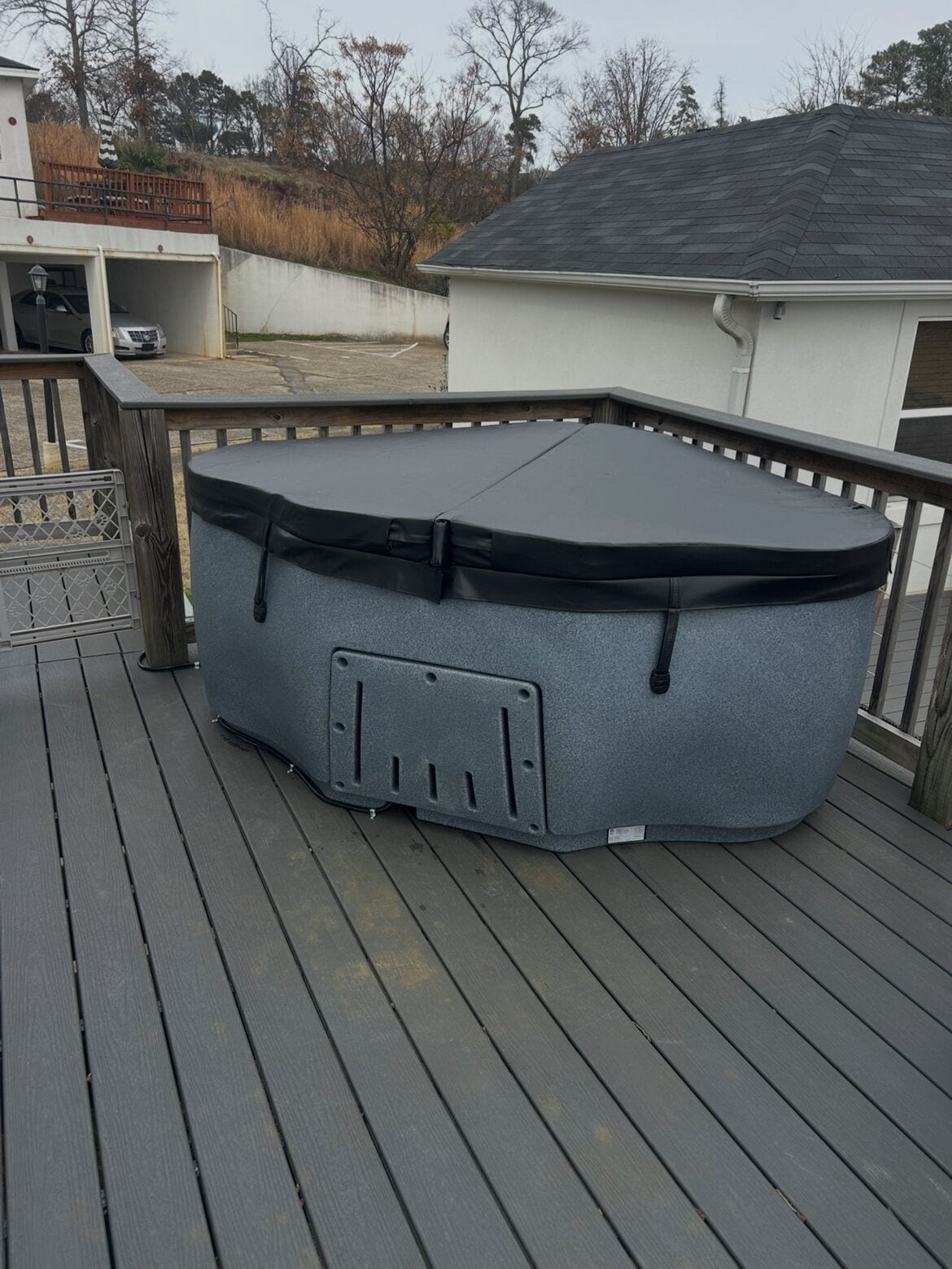 Un jacuzzi en una terraza de madera con un edificio blanco al fondo.
