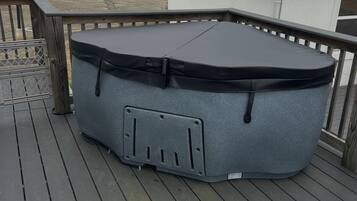 Un jacuzzi en una terraza de madera con un edificio blanco al fondo.