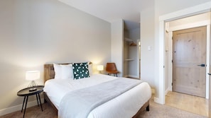 A hotel room with a bed, bedside tables, a chair, a wardrobe, and a door.