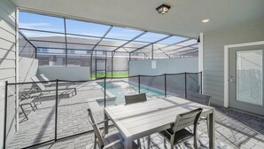 A covered patio area with a pool, a table and chairs, and a view of a house through a glass enclosure. - Windsor Island Dream | 5BR, 4.5 Bath Cozy Escape w/ Private Pool and Themed Kids' Rooms Near Disney (Davenport)
