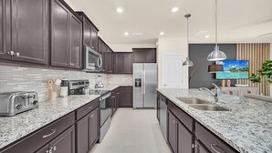 A modern kitchen with dark cabinets, granite countertops, stainless steel appliances, and a built-in oven. - Windsor Island Dream | 5BR, 4.5 Bath Cozy Escape w/ Private Pool and Themed Kids' Rooms Near Disney (Davenport)