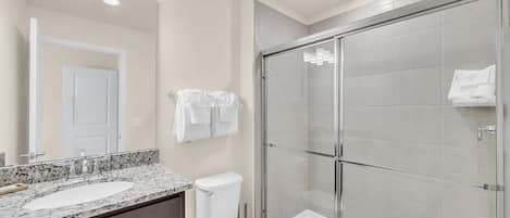 A bathroom with a glass-enclosed shower, a white toilet, and a marble sink.