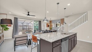 A modern kitchen with a large island, dark cabinetry, and pendant lighting. - Windsor Island Dream | 5BR, 4.5 Bath Cozy Escape w/ Private Pool and Themed Kids' Rooms Near Disney (Davenport)
