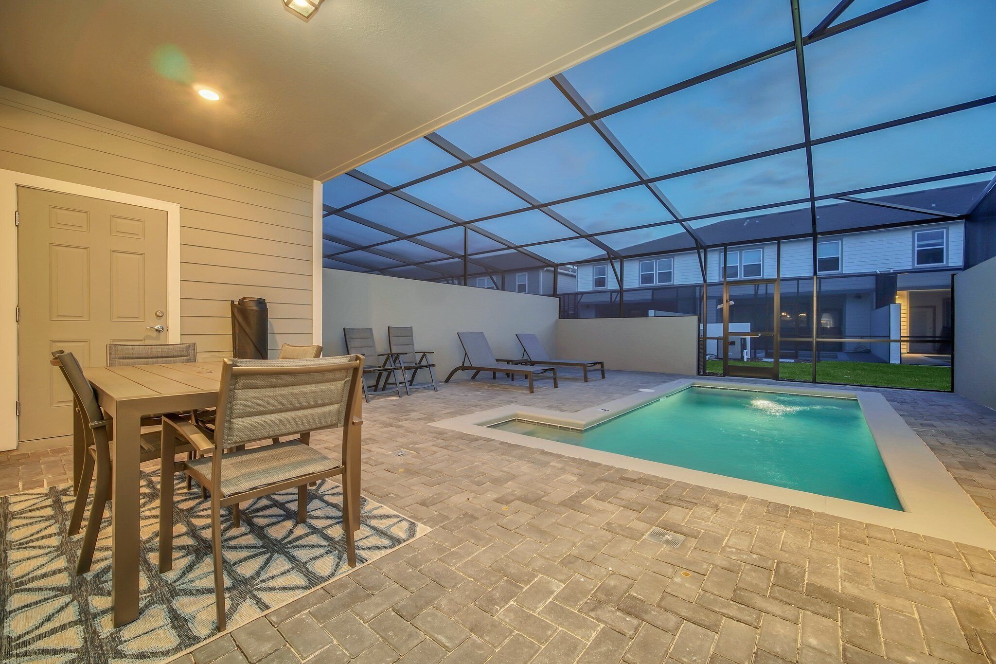 Un área de piscina interior con techo de vidrio, una mesa de comedor con sillas y una piscina pequeña.