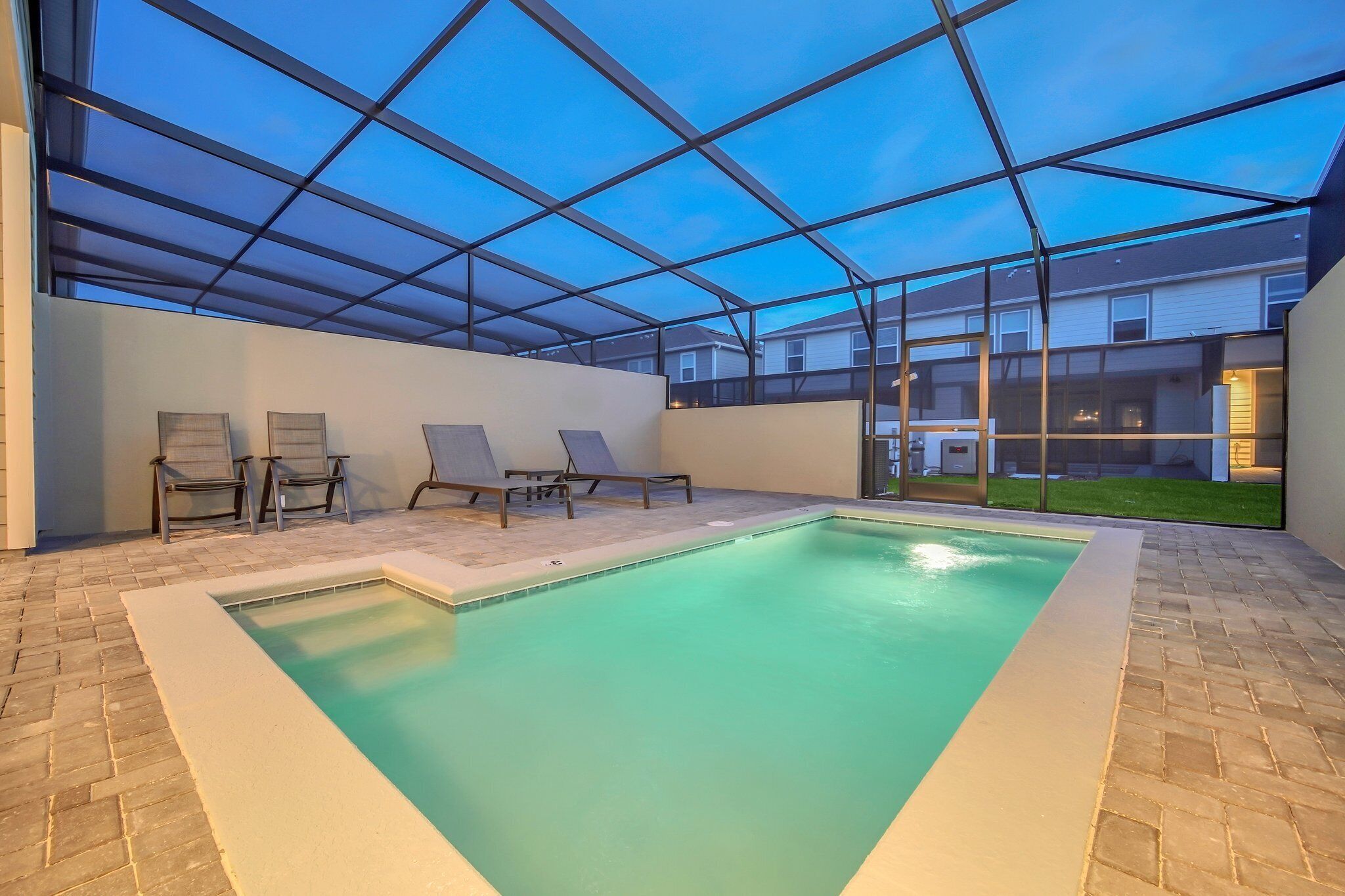 An indoor swimming pool with a glass ceiling, lounge chairs, and a view of residential buildings.