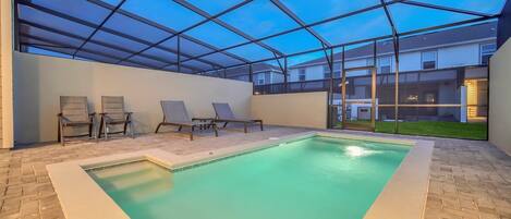 An indoor swimming pool with a glass ceiling, lounge chairs, and a view of residential buildings.