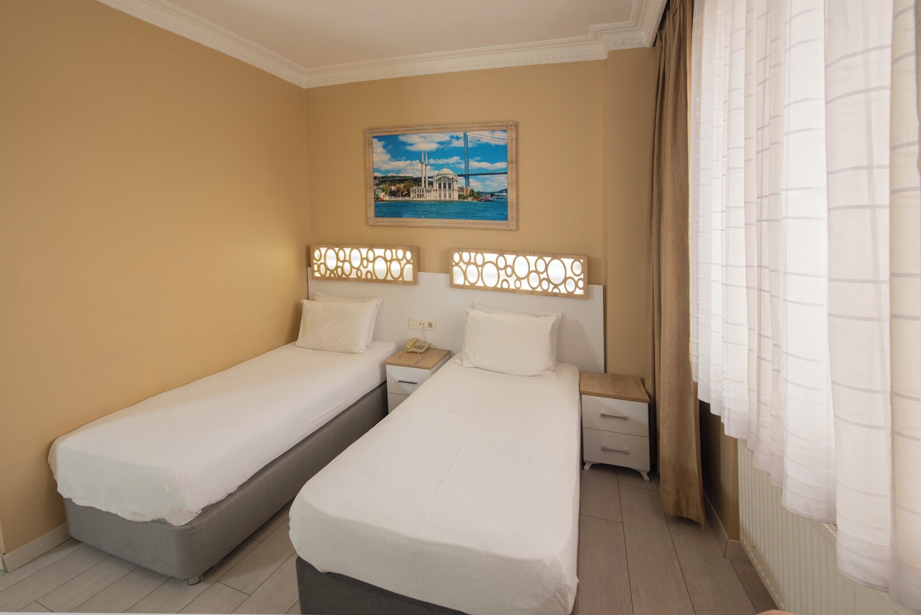 Une chambre d’hôtel avec deux lits simples, une table de chevet avec un téléphone et un tableau représentant un pont accroché au mur.