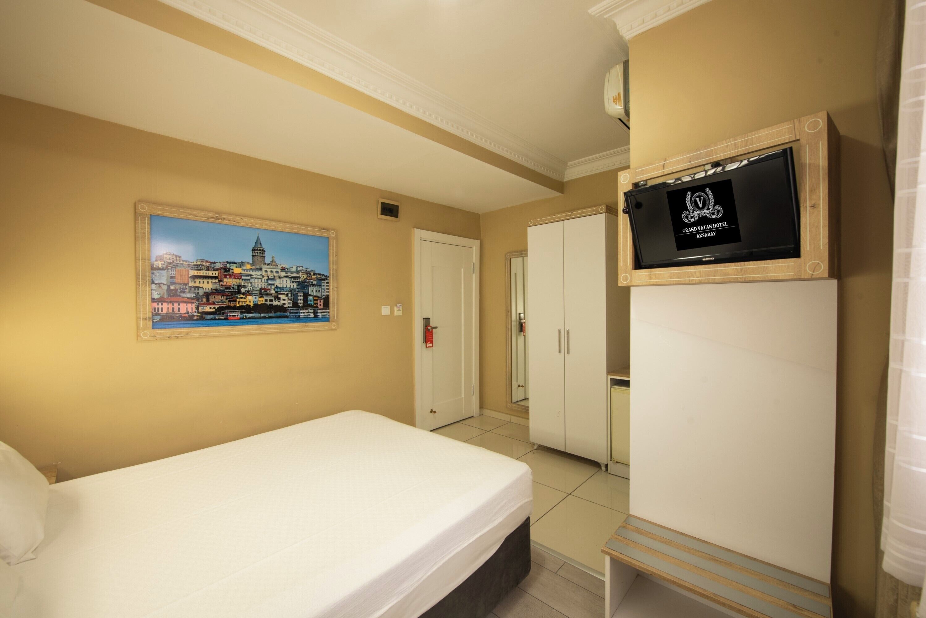 Una camera d'hotel con un letto, un armadio, una televisione e un dipinto con una veduta urbana.