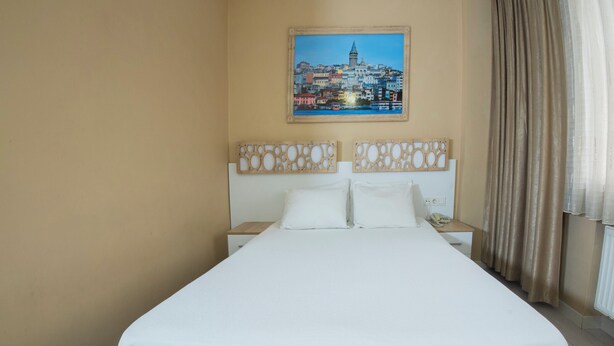 Une chambre d’hôtel avec un lit, une table de chevet, un téléphone et un tableau représentant un paysage urbain accroché au mur.