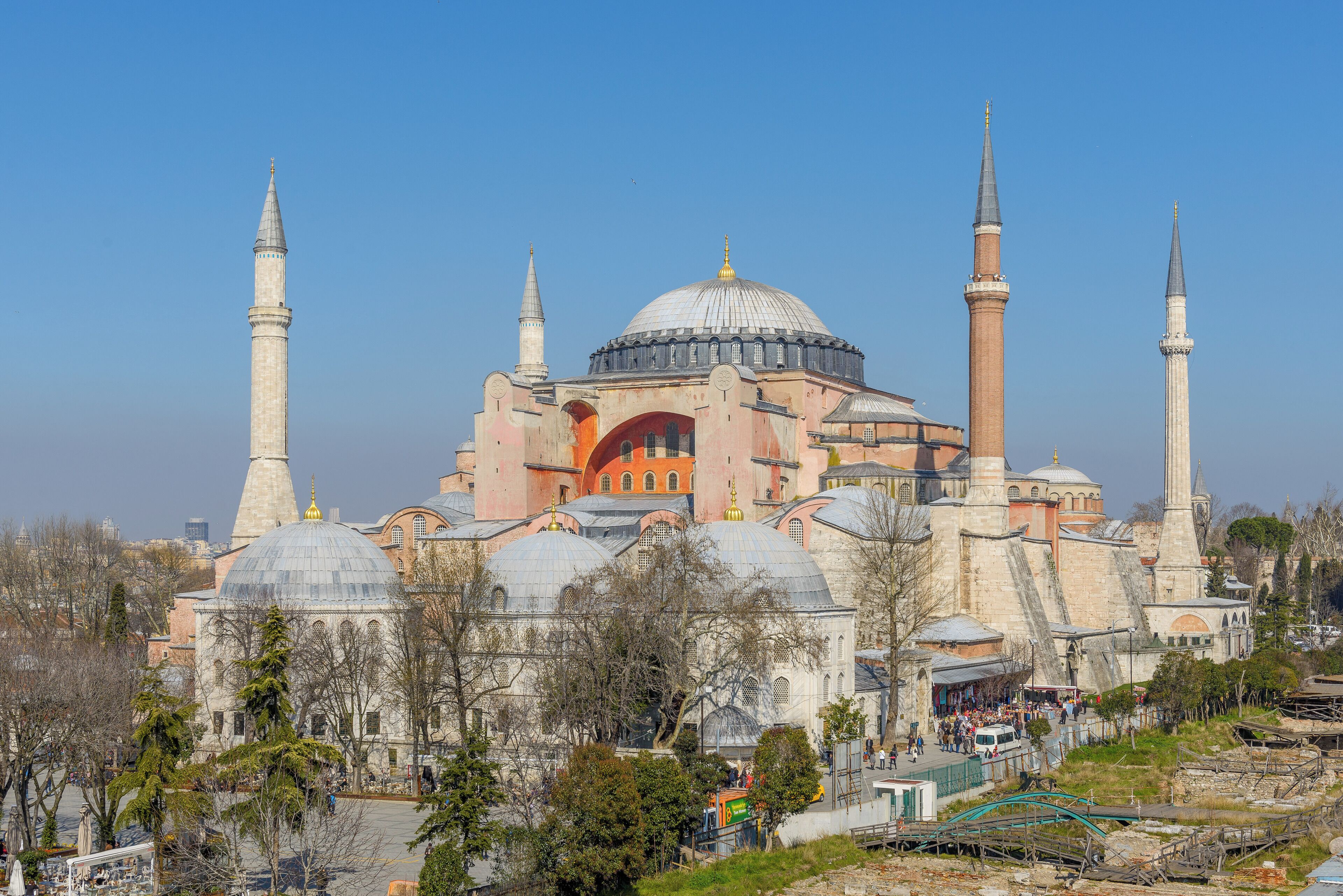 A large mosque with multiple domes and minarets, surrounded by trees and a busy street.