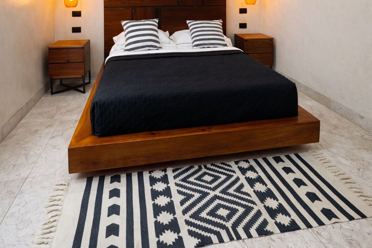 Quarto moderno com cama grande, ventoinha no teto, luminárias fixadas na parede e tapete estampado.