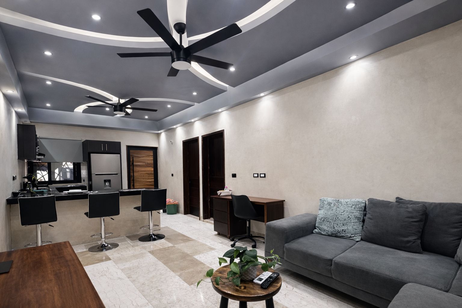 A modern living room with a grey sofa, a coffee table, and a dining area with chairs and a kitchen in the background.