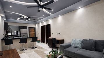 A modern living room with a grey sofa, a coffee table, and a dining area with chairs and a kitchen in the background.