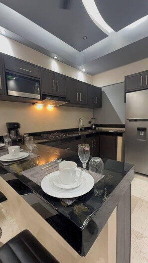 A modern kitchen with dark cabinets, a black marble island, and stainless steel appliances. - Kasa Nikte (Tulum)