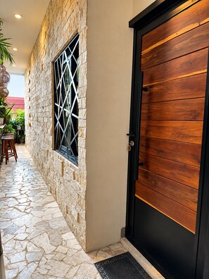 A stone exterior wall with a window, a black door, and a tiled walkway. - Kasa Nikte (Tulum)