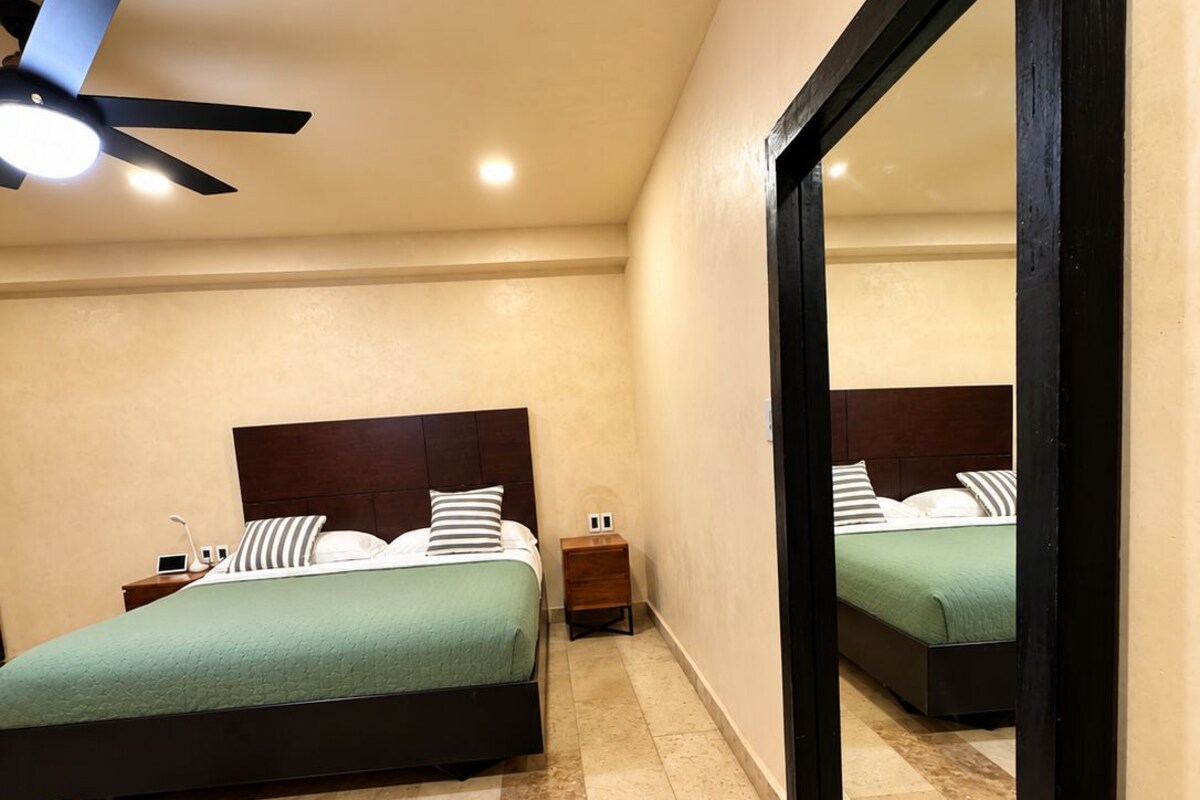 Quarto com cama, mesa de cabeceira e um espelho grande.