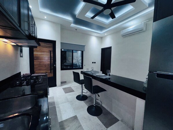 A modern kitchen with a central island, black bar stools, and a ceiling fan. - Kasa Nikte (Tulum)