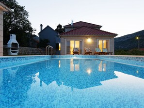 A swimming pool with a tiled edge, a stone wall, and a house with a red roof and two doors. - Villa Župa by Interhome (Zagvozd)