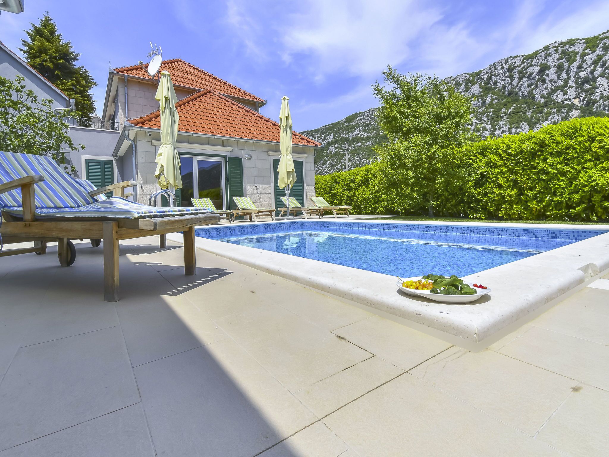 Zona de piscina con sillones de descanso y una mesa de comedor con un plato de fruta.