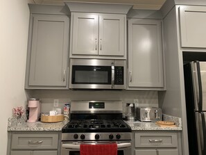 A kitchen with grey cabinets, a stainless steel microwave, a gas stove, and a refrigerator.
