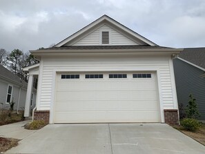 A single-story house with a white garage door, a brick foundation, and a sloped roof.