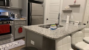 A modern kitchen with a granite countertop, stainless steel appliances, and a built-in island with seating. - Cozy Southern Retreat, 4 Spacious Bedrooms, Massage Chair, 8 Mins to Ole Miss (Oxford)