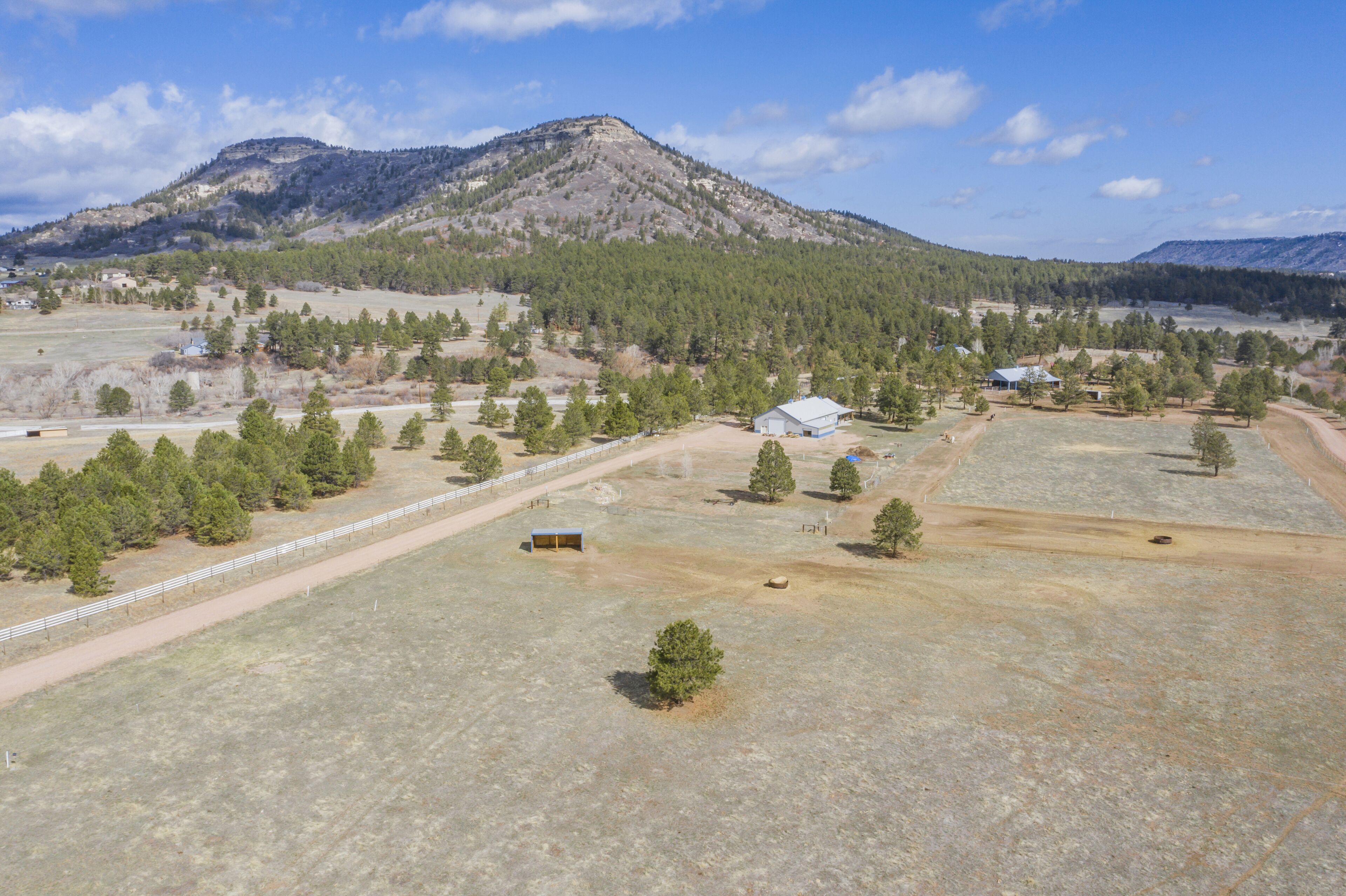 An aerial view of a rural area with a mountain in the background, a fenced field, and several buildings.