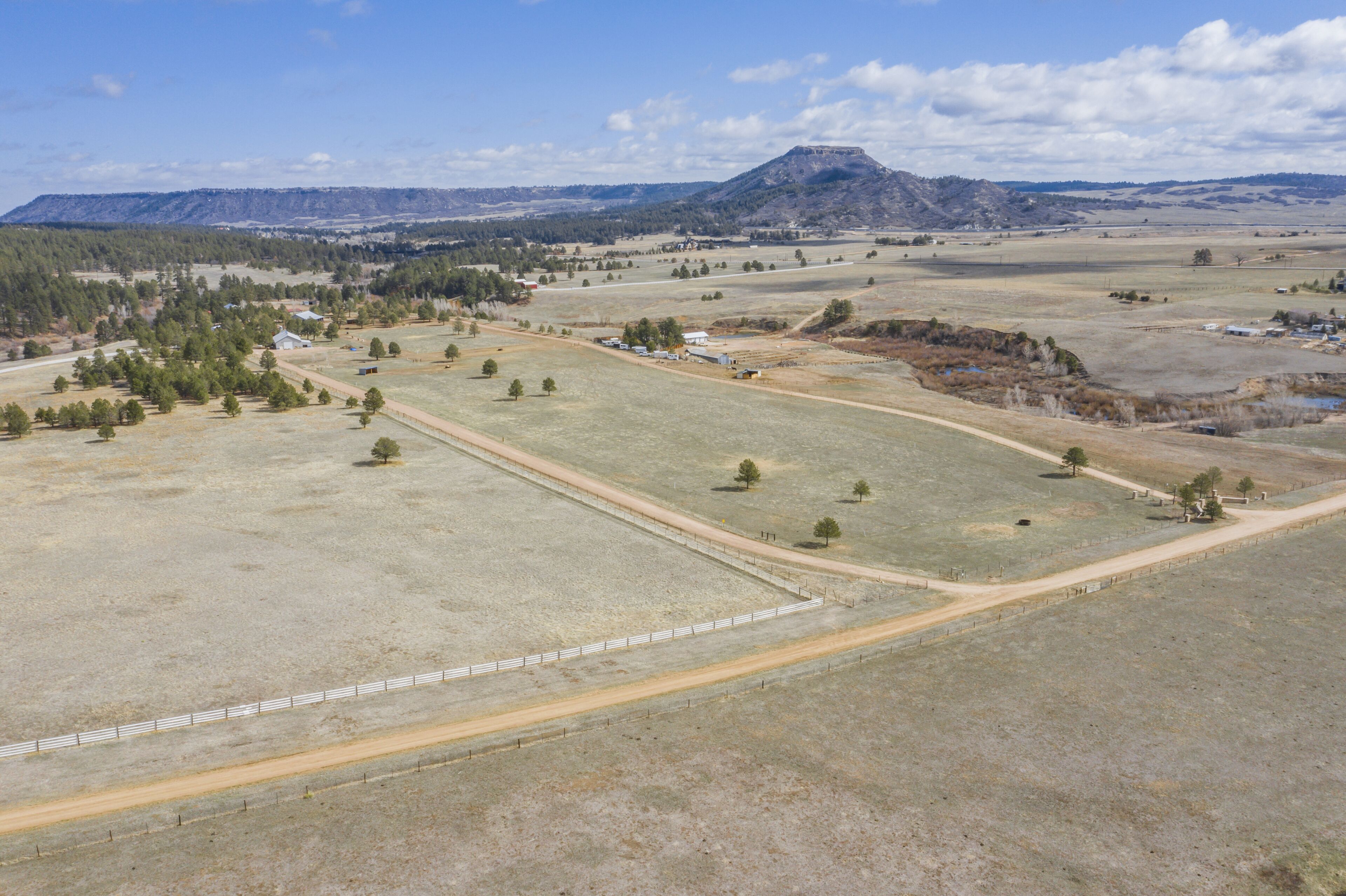 An aerial view of a rural landscape with fields, a few scattered buildings, and a prominent hill in the background.