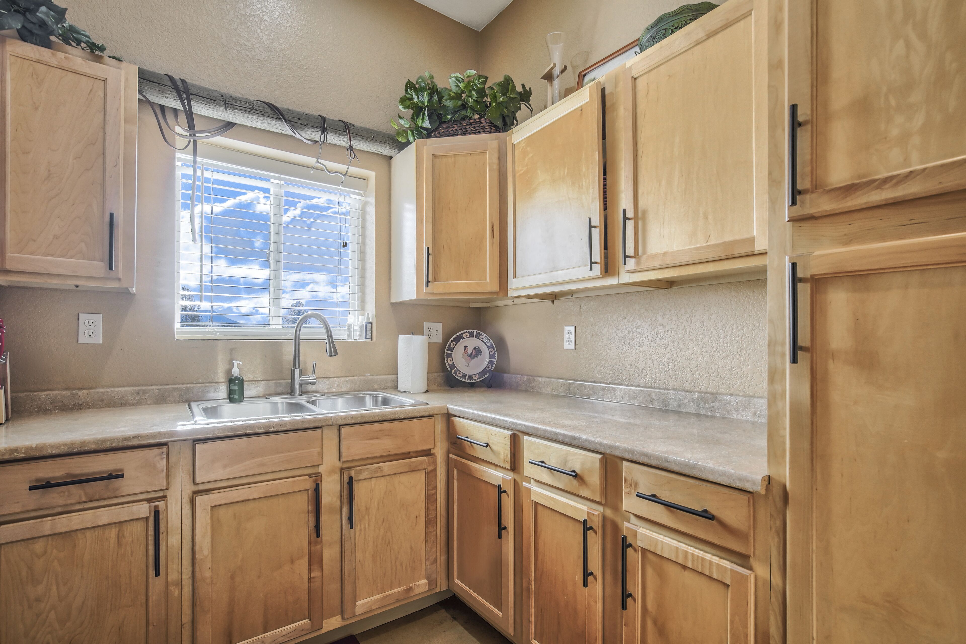 A kitchen with wooden cabinets, a sink, and a window with blinds.