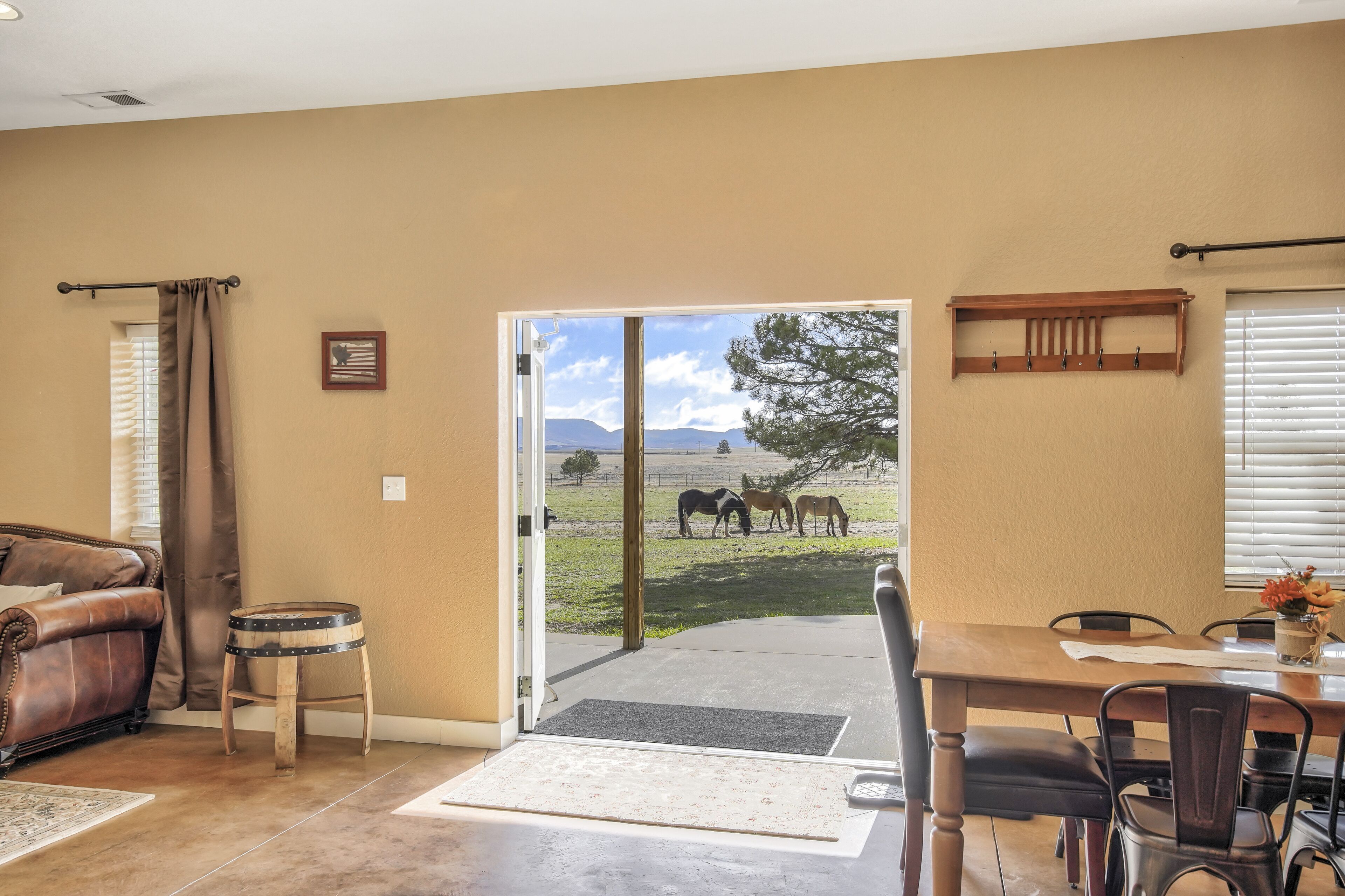 A room with a door leading to a patio where horses are grazing.