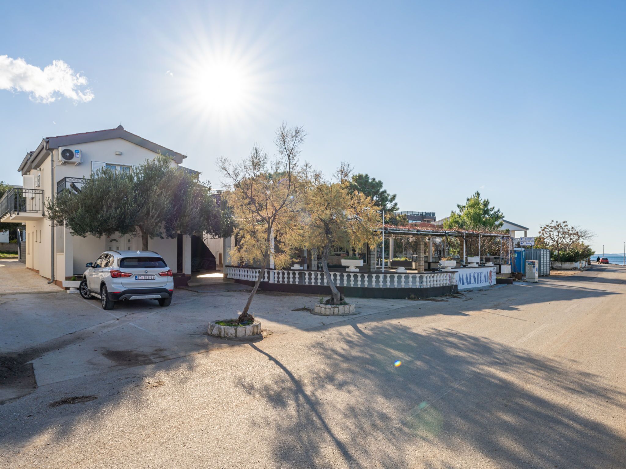 A residential area with a white car parked in front of a house, a covered outdoor seating area, and a clear sky.