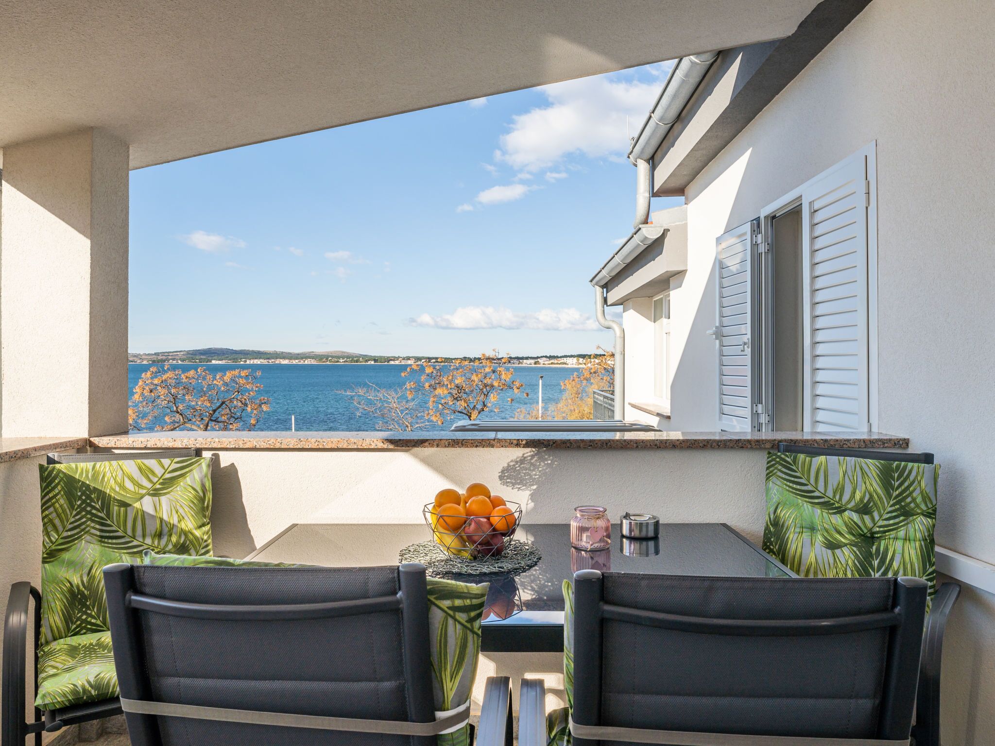 A balcony with a table and chairs, a view of the sea, and a bowl of fruit.