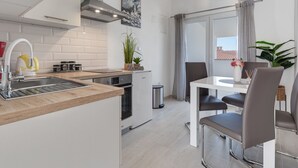 A modern kitchen with a built-in island, a dining area with a white table and chairs, and a view of the city through large windows. - Tramonto by Interhome (Vir)