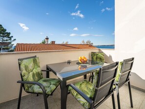 A balcony with a table and chairs, a view of the sea, and a building with a red-tiled roof. - Tramonto by Interhome (Vir)