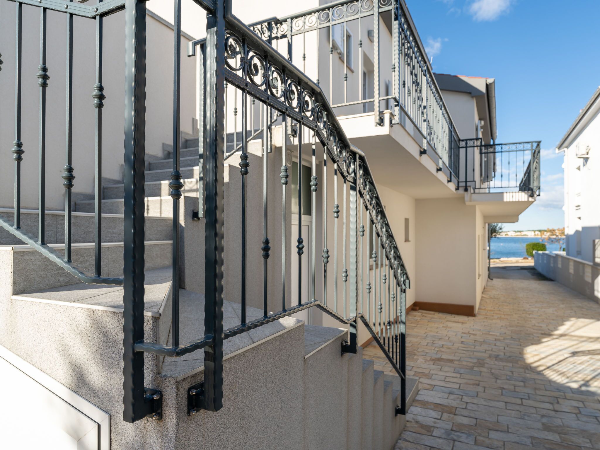 Un escalier avec des rampes en métal noir menant à un bâtiment blanc doté de balcons.