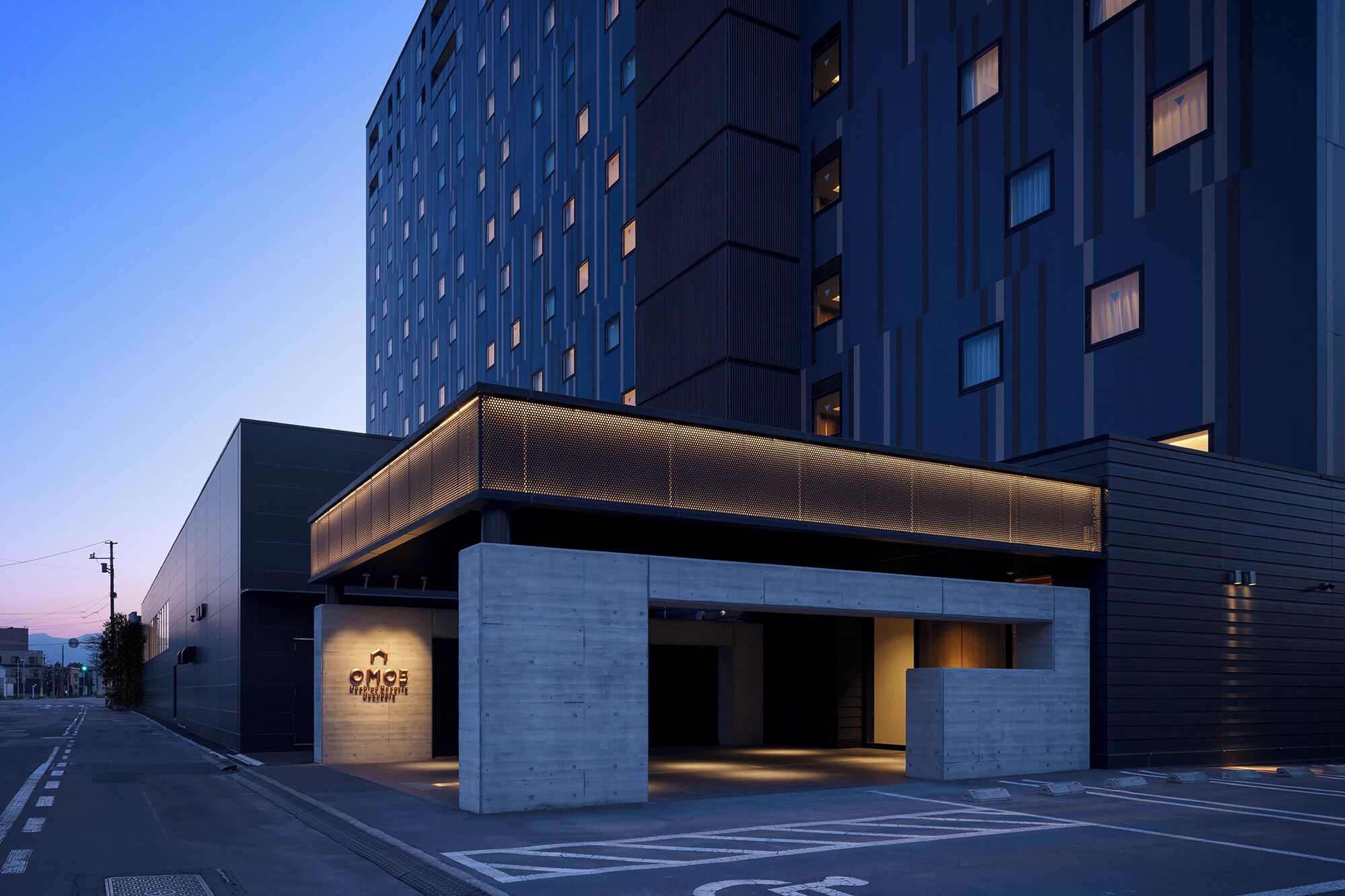 A modern hotel entrance with a covered walkway, concrete pillars, and a sign with the hotel name.