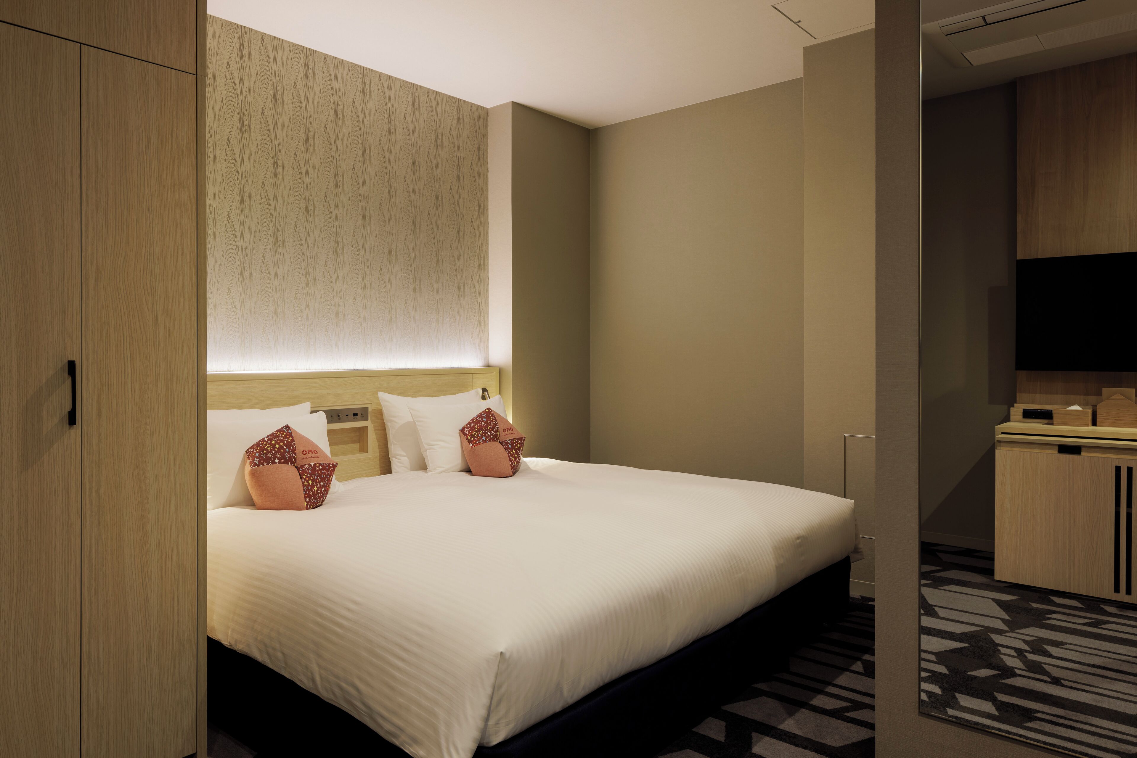 A hotel room with a large bed, a wooden wardrobe, a television, and a small desk.