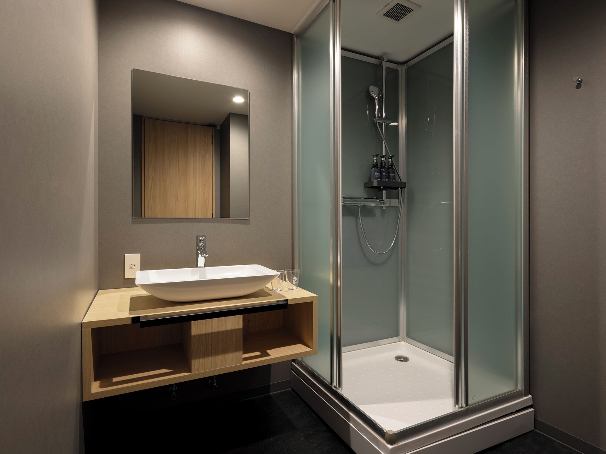 Een moderne badkamer met een grote spiegel, een wastafel op een voetstuk en een douche met glazen wanden.