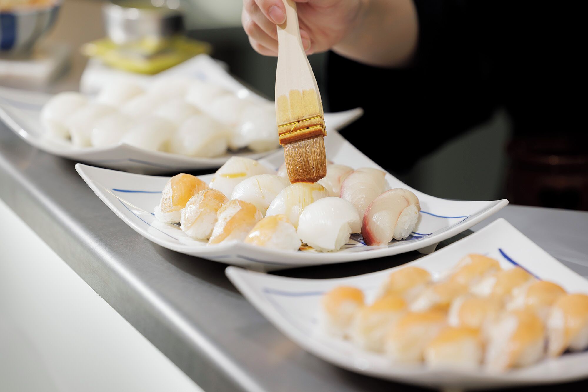 En person bruger en pensel til at påføre sauce på sushi på en tallerken.