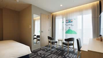 A hotel room with a bed, two chairs, a small table, a desk, and a large window with curtains.