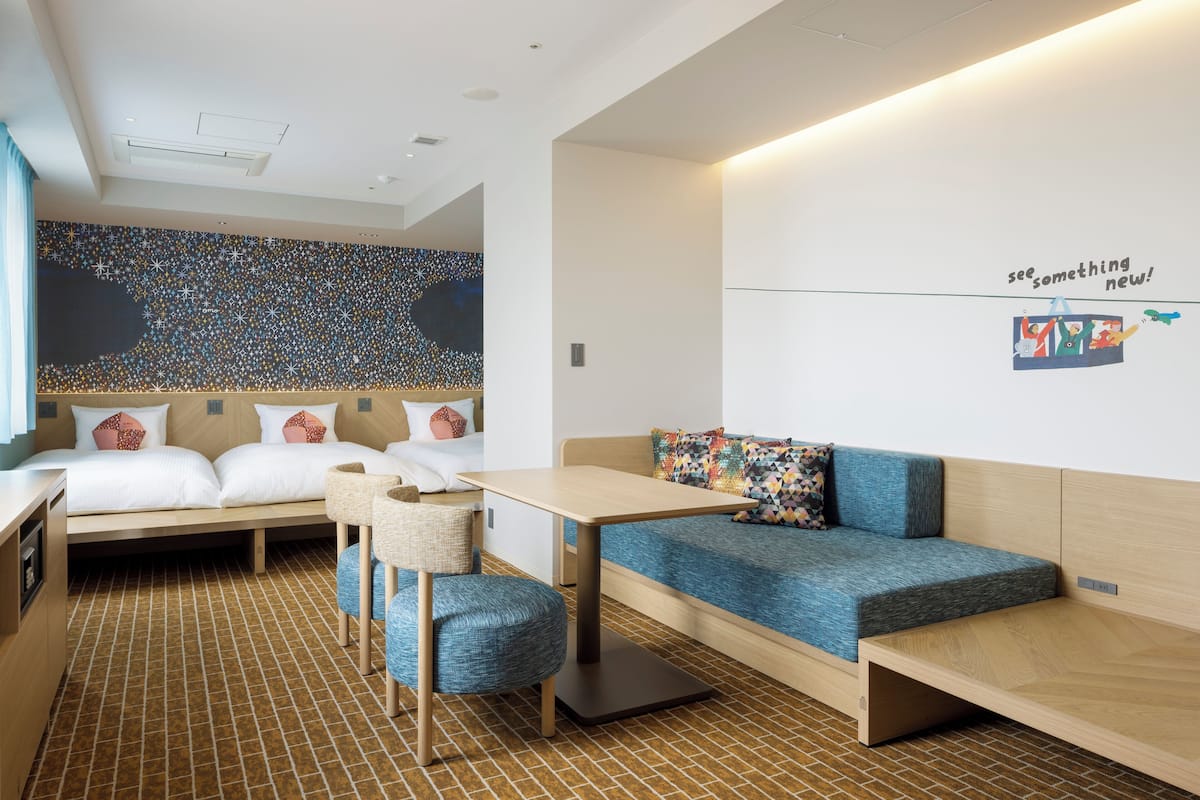 Une chambre d’hôtel moderne équipée d’un lit, d’un canapé, d’une petite table et d’un mur orné d’une citation inspirante.