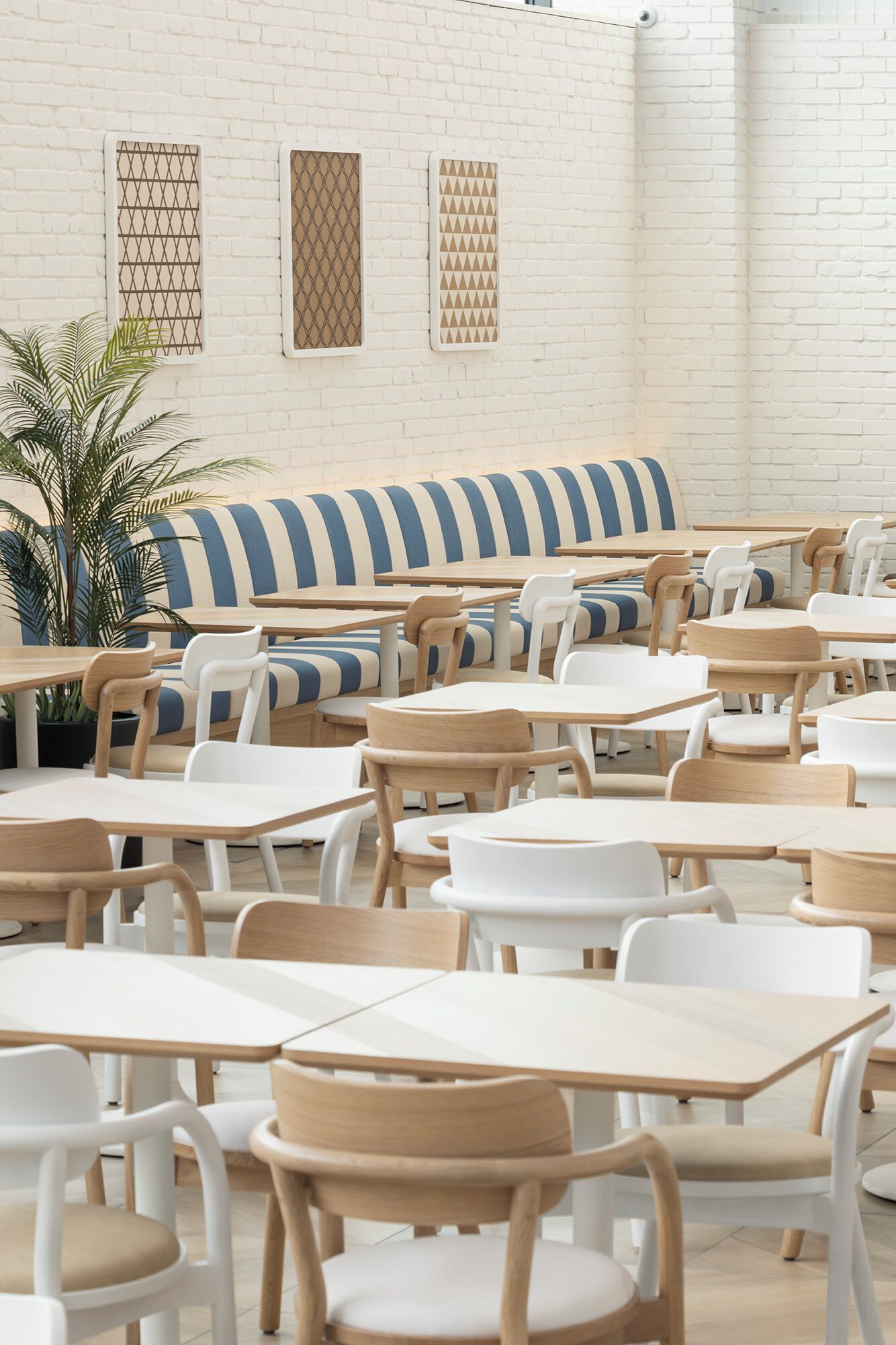 A spacious indoor seating area with multiple tables and chairs, a striped bench, and a potted plant.