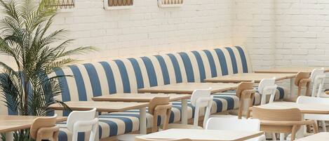 A spacious indoor seating area with multiple tables and chairs, a striped bench, and a potted plant.