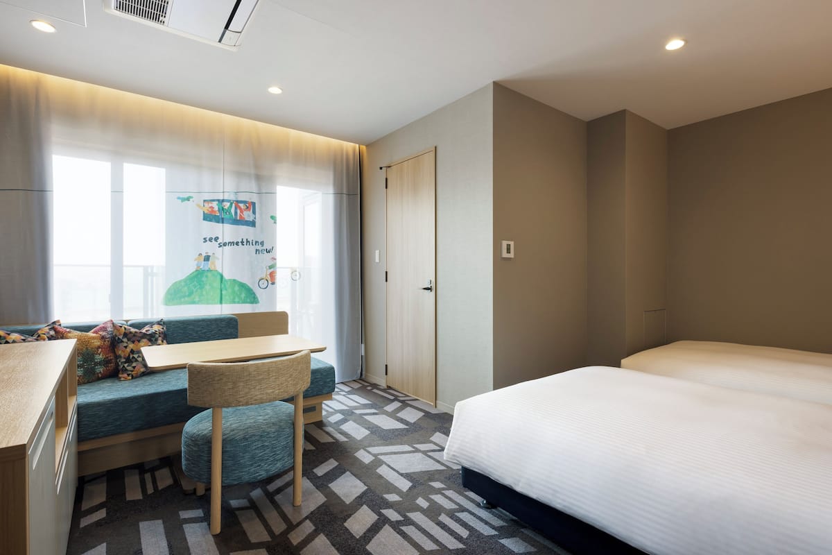 Une chambre d’hôtel avec un lit, un bureau et une chaise, un canapé et une fenêtre avec des rideaux.