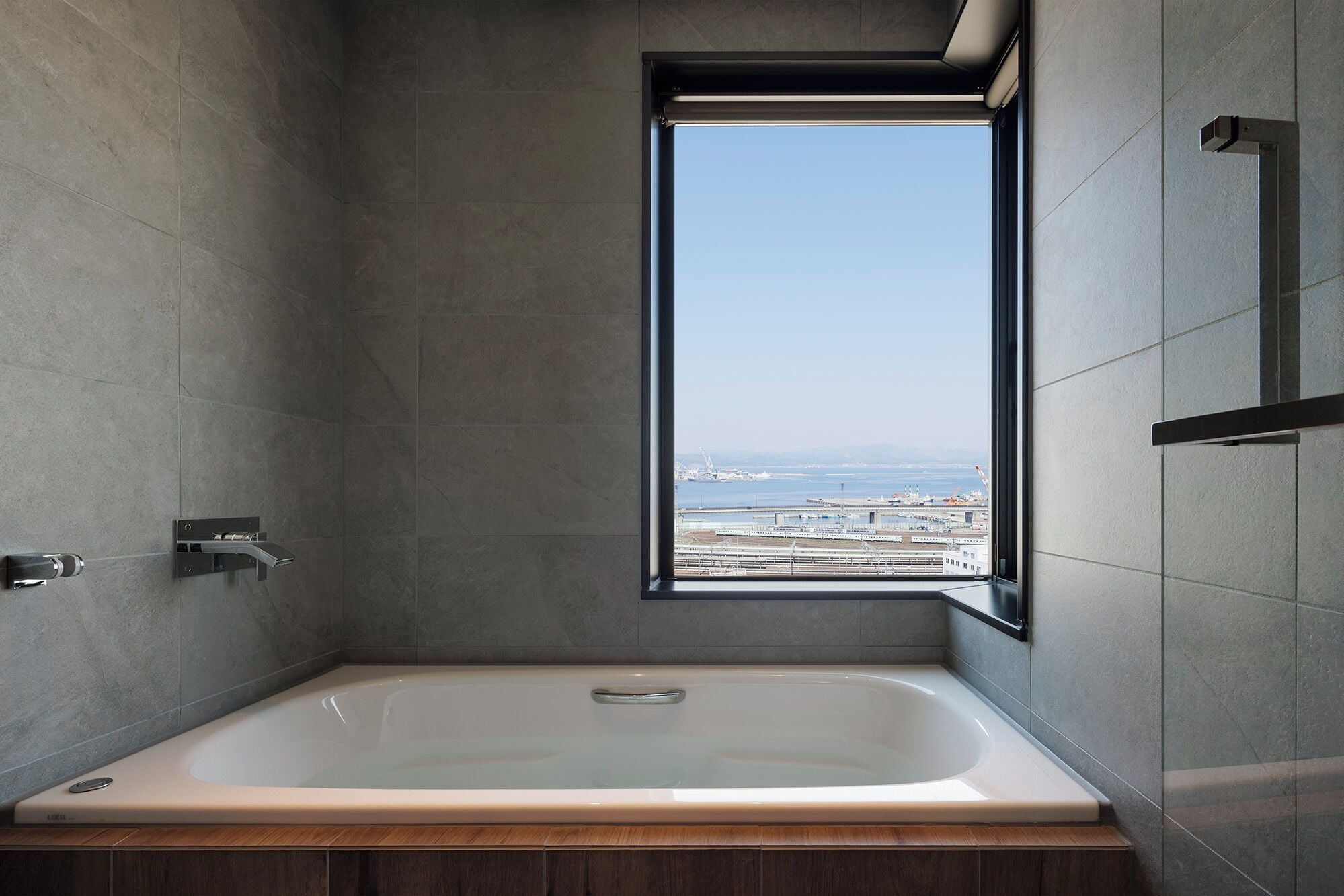 Un baño moderno con una bañera amplia, una ventana con vistas a la playa y una zona de ducha.