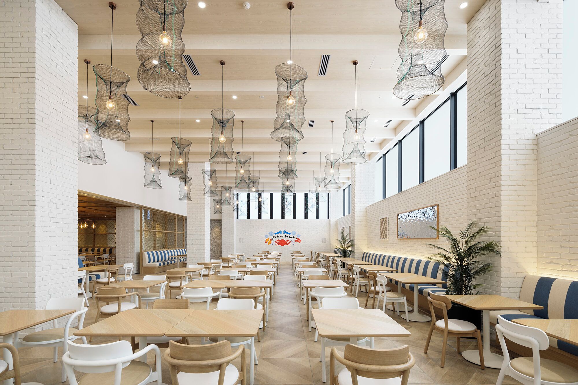 En rummelig restaurant med højt til loftet, hængende pendellamper og et centralt siddeområde med borde og stole.