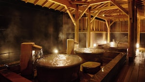 Un bain traditionnel en bois, doté de grandes baignoires en pierre et où s’élève une vapeur d’eau.