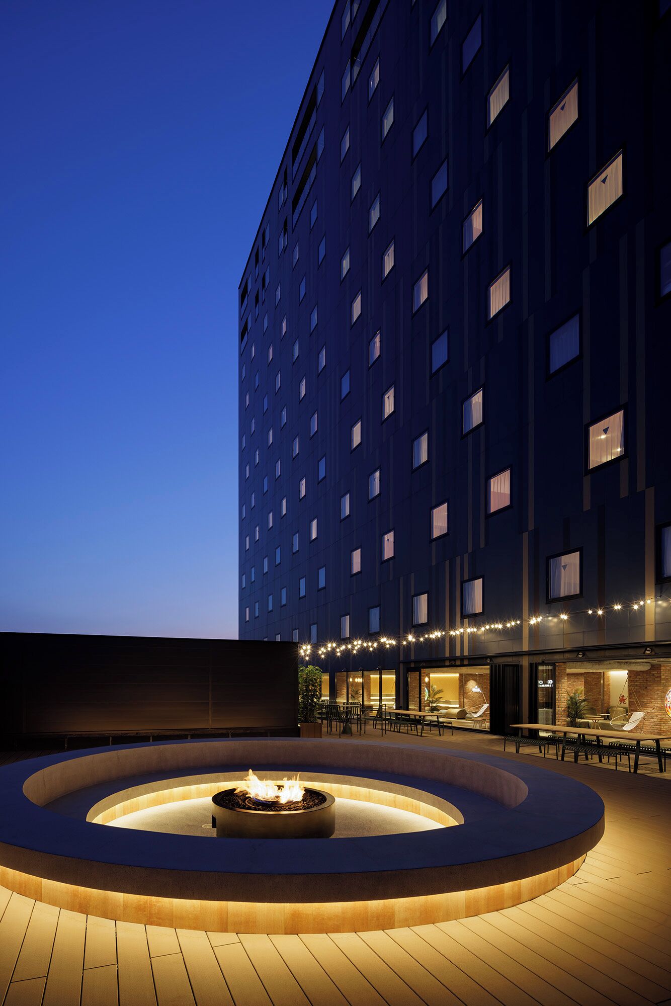 A modern hotel exterior at dusk with a circular outdoor seating area and a fire feature.