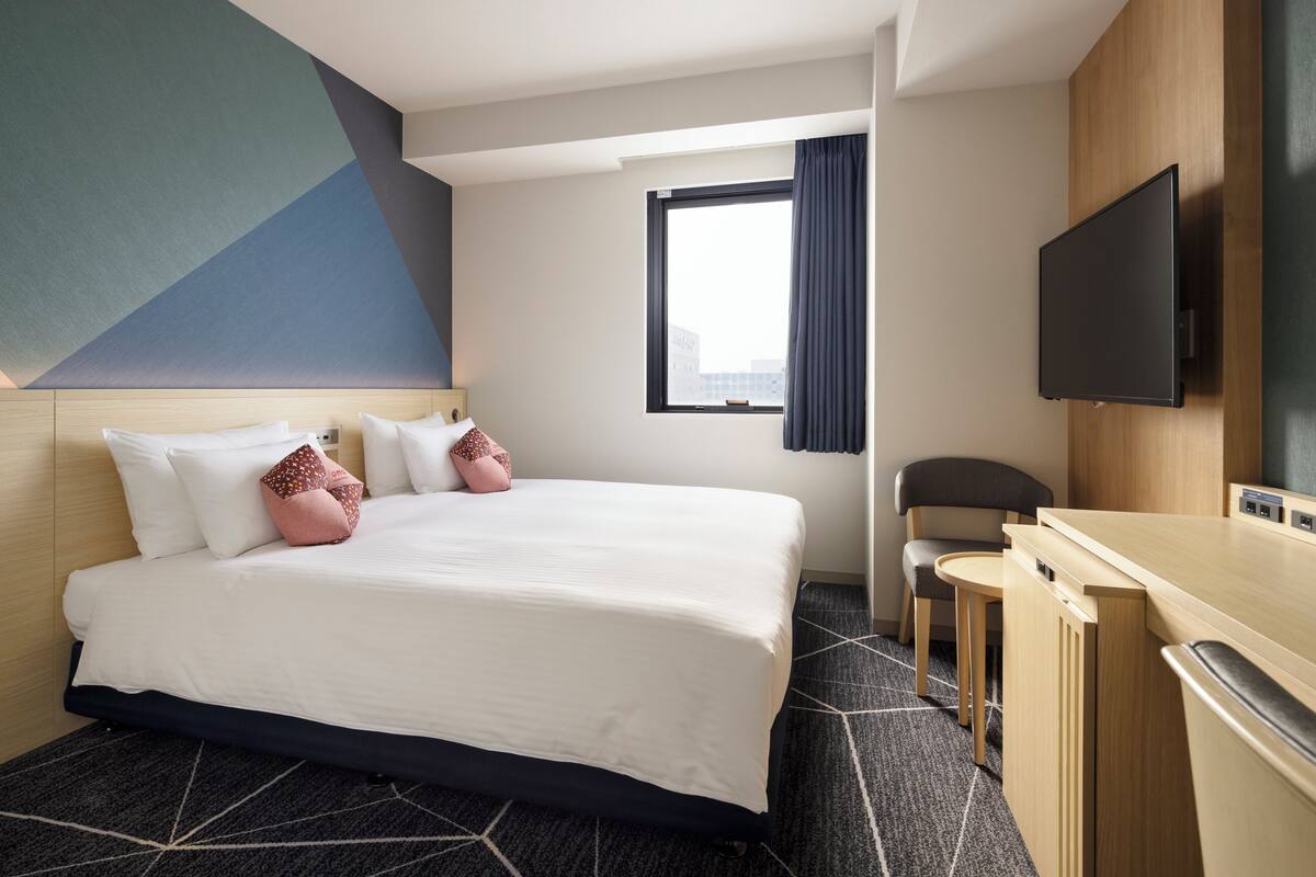 Une chambre d’hôtel avec un grand lit, un bureau, une chaise, un téléviseur à écran plat et une fenêtre avec des rideaux.
